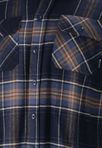 Marineblauwe flanel shirt met een bruine en blauwe geruite patroon, met twee borstzakken en blauwe knopen. Zachte textuur, klassiek ontwerp.