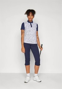 Granatowo-biały strój golfowy, składający się z koszulki z kołnierzykiem z kwiatowym wzorem i jednolitymi rękawami, zestawiony z granatowymi kapri o długości do kolan.