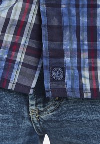 Karobluse aus Baumwolle mit blauen, grünen und roten Streifen, einem marineblauen Saum und einem Logo-Patch. Kombiniert mit blauen Denim-Jeans.