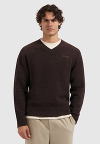 Bruine v-hals trui met ribbelmanchetten en -zoom. Zachte textuur en getailleerde stijl. Bevat subtiele logodetail in lichter bruin op de borst.