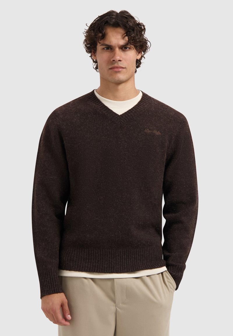 Bruine v-hals trui met ribbelmanchetten en -zoom. Zachte textuur en getailleerde stijl. Bevat subtiele logodetail in lichter bruin op de borst.