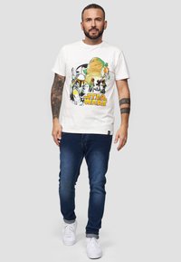 Weißes Baumwoll-T-Shirt mit "Star Wars"-Grafik, die Charaktere in Grün, Orange und Schwarz zeigt. Kombiniert mit dunkelblauen Jeans und weißen Turnschuhen.