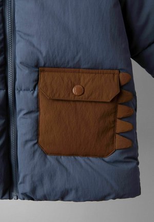 Blauwe gewatteerde jas met een bruine klepzak met een knoop en decoratieve driehoekige stoffen accenten aan de rechterkant.