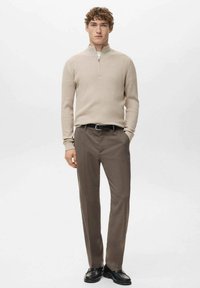 Beiger, gerippter Strickpullover mit einem Viertel-Reißverschluss, kombiniert mit dunkelbraunen, maßgeschneiderten Hosen und schwarzen Lederschuhen. Einfaches, modernes Design.