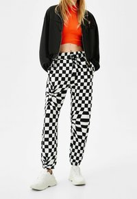 Svart och vit rutiga byxor med elastiska fållar, i kombination med en åtsittande orange topp och en svart bomberjacka. Vita sneakers fulländar looken.