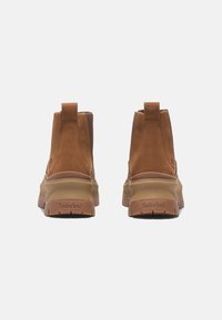 Bruna mockaskor med gummisula, som har en dragflik bak och en strukturerad ovandel. Timberland-logotypen syns på hälen.
