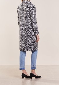 Leopardprint jas in zwart en wit, middenlange ontwerp met lange mouwen en een notch-kraag, gecombineerd met lichtblauwe jeans en zwarte hakken.