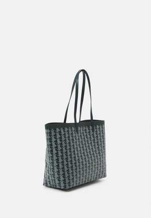 Sac fourre-tout en matériau vert foncé avec un motif géométrique blanc. Comprend deux longues poignées et un design spacieux à ouverture supérieure.