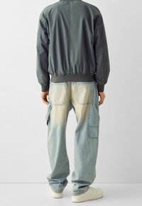 Grå bomberjacka med en åtsittande midja, tillsammans med ljusblå, avslappnade jeans med gradientblekning och stora sidofickor.