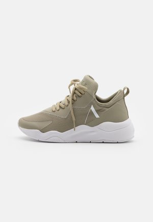 Beiger Mesh-Sneaker mit dicker weißer Sohle, gepolstertem Knöchelkragen, Schnürung vorne und einem kleinen weißen schrägen Streifen an der Seite.