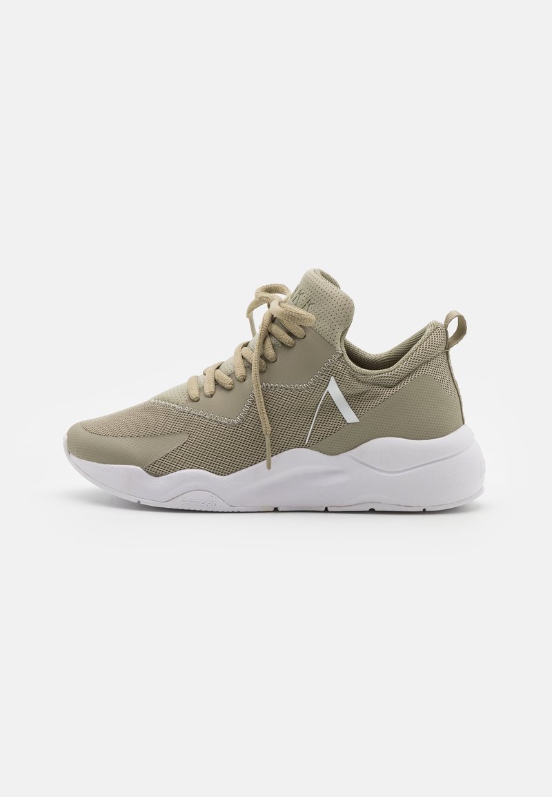 Baskets en mesh beige avec semelle blanche épaisse, col matelassé à la cheville, laçage à l'avant et une petite bande blanche en biais sur le côté.