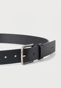 Μαύρη δερμάτινη ζώνη με υφή, αγκράφα σε ασημί τόνο και τρύπες για ρύθμιση. Διαθέτει απλό και κομψό σχέδιο.