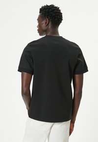 Sort kortærmet T-shirt lavet af glat bomuld med rund hals. Har en afslappet pasform og en diskret ribbet tekstur på ærmerne.