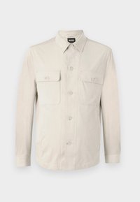Cămașă butonată de culoare bej deschis, cu mâneci lungi, două buzunare frontale și guler clasic. Realizată dintr-un material neted, cu o croială lejeră.