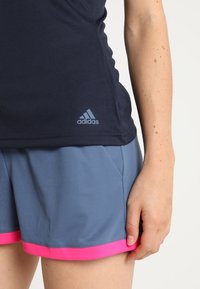 Granatowy strój sportowy z logo adidas i jasnoniebieskimi akcentami, połączony z szarymi szortami o siateczkowej teksturze i różowym wykończeniu.