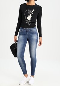 Black long-sleeve shirt with a bear graphic, blue skinny jeans, white slip-on shoes, and a textured black handbag.