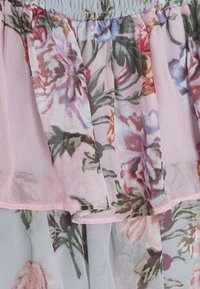 Kukkakuvioinen mekko läpikuultavasta kankaasta; siinä on vaaleanpunaisia sävyjä, kerroksellisia röyhelöitä ja monimutkaisia kukkakuoseja punaisilla, sinisillä ja vihreillä yksityiskohdilla.