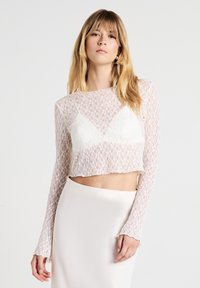 Cropped top in pizzo bianco con maniche lunghe, caratterizzato da un sottopunto triangolare e orli a scallop, abbinato a una gonna in satin bianco liscia.