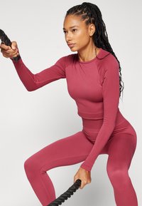 Burgundy hosszú ujjú crop top és passzoló, magas derekú leggings sima, rugalmas anyagból, bordázott textúrával és karcsú szabással.