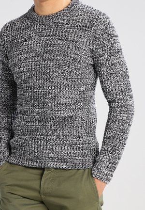 Pull en tricot noir et blanc avec un motif texturé, doté d'un col rond et de manches longues. Assorti avec un pantalon vert clair.