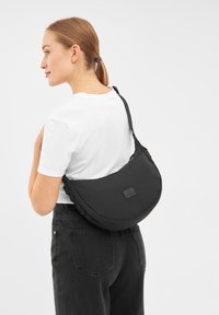Borsa a spalla in tessuto nero con design arrotondato, caratterizzata da una texture imbottita, una tracolla regolabile e un piccolo patch con logo sulla parte anteriore.