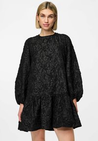 Vestido negro con un patrón texturizado y arrugado, mangas largas tipo globo y un dobladillo acampanado y en capas. Tejido suave y ligero.