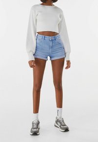 Vit ribbad kort tröja, högmidjade ljusblå denimshorts och grå sneakers med vita detaljer. Standard passform med uppvikta shorts.