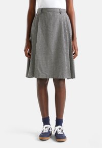 Kraťasová sukně do délky kolen v černobílém vzoru houndstooth, s plisovaným designem a přiléhavým pasem. V kombinaci s modrými teniskami.