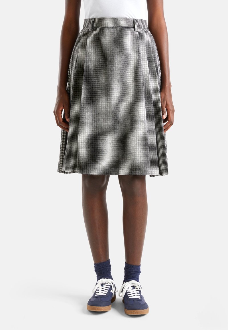 Kraťasová sukně do délky kolen v černobílém vzoru houndstooth, s plisovaným designem a přiléhavým pasem. V kombinaci s modrými teniskami.