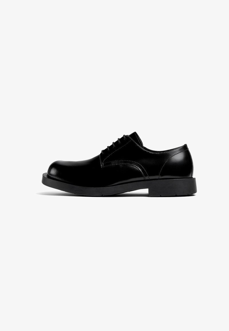 Zapato negro de cuero con cordones, punta redondeada, acabado liso y suela de goma. Presenta detalles de costura en los laterales y la lengüeta.