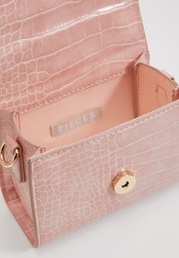 Borsa a tracolla rosa con motivo coccodrillo e texture liscia. L'interno è rivestito con un morbido tessuto e presenta un'etichetta con la scritta "PIECES." Dotata di chiusura a scatto dorata.