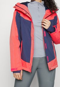 Färgglad jacka med en blandning av ljus korall och marinblå paneler, tillverkad av lätt material, med komfortabel passform och justerbar huva.