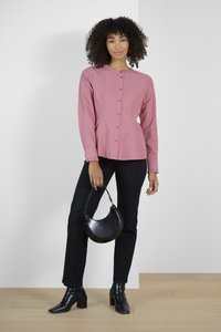Blouse rose à manches longues, avec un col rond et de subtils froncés aux poignets. Associée à un jean noir et un sac à main noir à forme arrondie.