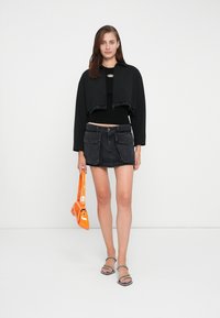 Zwarte cropped jack met rafelige randen, zwart geribbeld topje, donkerdenim minirok, oranje lakleren handtas en sandalen met doorzichtige bandjes.