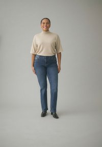Beige, kortärmad polotröja med avslappnad passform, kombinerad med blå denimjeans med raka ben och svarta ankelstövlar med klack.