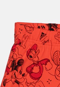 Shorts in cotone arancione con grafiche nere in stile cartoon di Topolino e Paperino, dotati di una cintura elastica e branding Adidas.