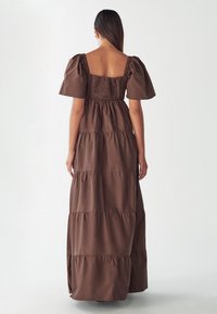Brown tiered maxi dress with short puff sleeves, square back, and smocked details, made of soft, textured fabric.