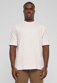 Lyserød bomulds t-shirt med korte ærmer og hvide detaljer ved ærmekanterne. Løs pasform og rund halsudskæring. Enkel design.