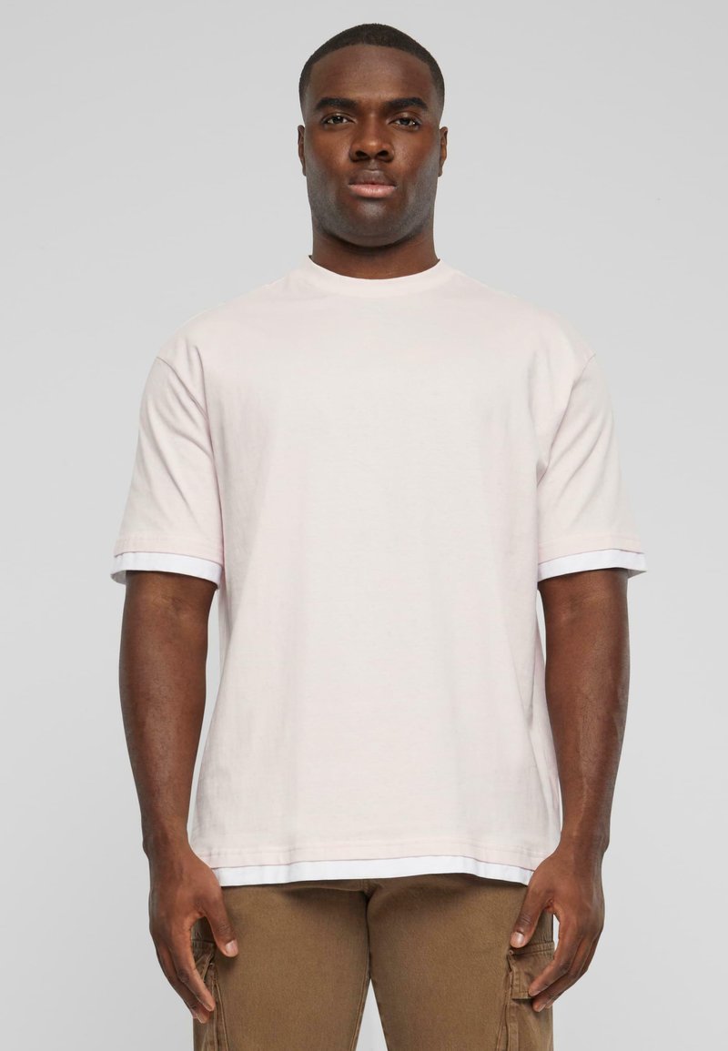 Lyserød bomulds t-shirt med korte ærmer og hvide detaljer ved ærmekanterne. Løs pasform og rund halsudskæring. Enkel design.