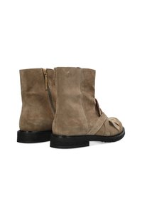 Bottines en suede marron avec une fermeture éclair, semelle en caoutchouc noir et straps décoratifs à l'avant. Fini texturé avec un aspect mat.