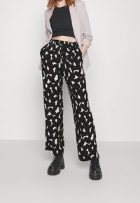 Zwarte wijde broek met een wit abstract patroon, voorzien van een trekkoord in de taille en zijzakken. Draag met een zwarte cropped top en een lichte blazer.