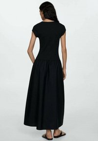 Robe noire avec un haut ajusté à manches courtes et une jupe fluide longueur cheville avec une taille froncée. Tissu lisse et design épuré.