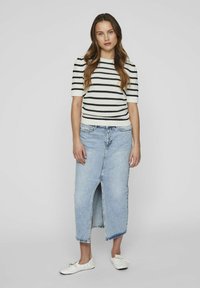 Top de punto negro con rayas blancas, falda midi de mezclilla azul con abertura frontal y zapatillas blancas. Materiales texturizados y diseño ajustado.