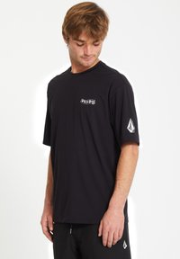 T-shirt nera a maniche corte realizzata in tessuto morbido. Presenta un piccolo logo frontale e un logo distintivo sulla manica sinistra.