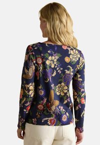 Długi rękaw granatowa bluzka z kolorowymi wzorami kwiatowymi i ptakami, o gładkiej teksturze i luźnym kroju. Tylny widok z okrągłym dekoltem.