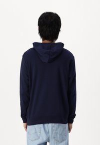 Sudadera azul marino con capucha, mangas largas y puños acanalados, vista desde la parte posterior. Diseño simple y sólido sin patrones ni detalles de hardware.