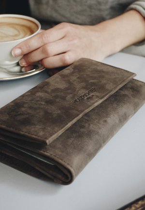 Brown suede wallet with embossed logo. Folded design features stitching detail and a smooth texture, placed next to a coffee cup.