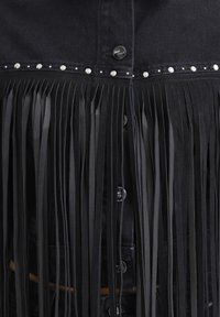 Black denim jacket section with silver studs along upper seam and long black leather fringe hanging below buttons.