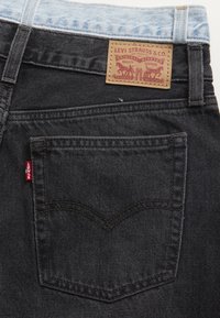 Mörka denimjeans med ett ljusblått midjeband, med en brun läderlapp på baksidan, röd Levi's-tagg och klassisk design på bakfickorna.