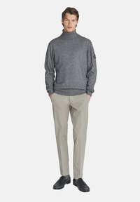 Maglione a collo alto grigio con un lavorazione a maglia testurizzata, abbinato a pantaloni grigi chiari e scarpe nere. L'outfit è semplice e aderente.